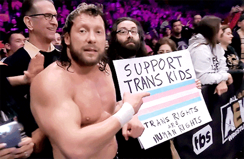 a shirtless man holds a sign that says support trans kids