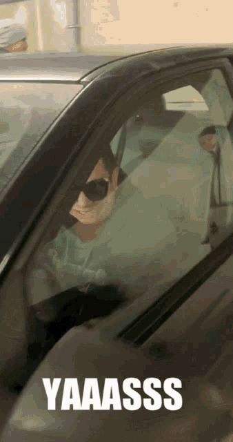 a man wearing sunglasses is sitting in a car with the words yaaass on the side