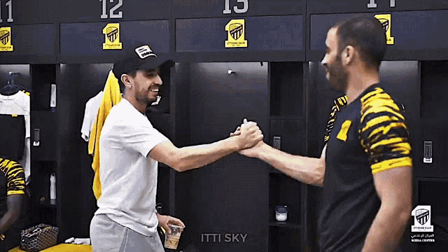 two men shaking hands in a locker room with a sign that says itti sky on it