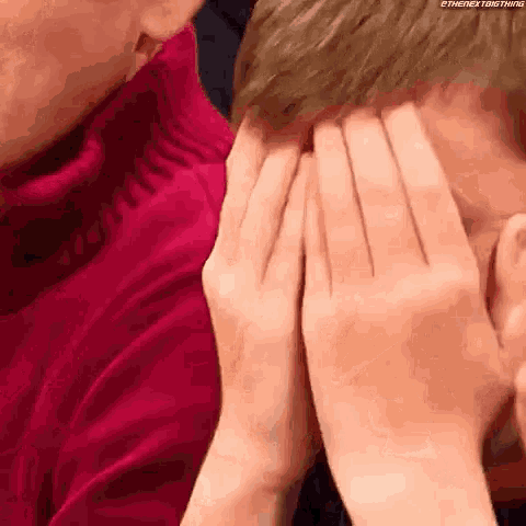 a person is covering their face with their hands while another person looks on .