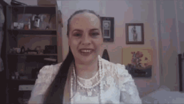 a woman wearing a white lace top and pearls is smiling while sitting in a room .