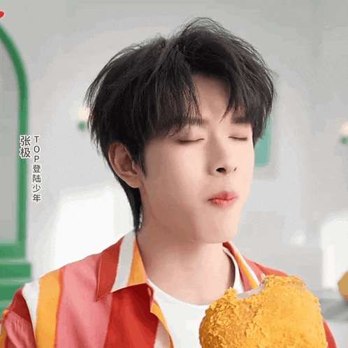 a young man with chinese writing on his shirt is eating a fried chicken breast