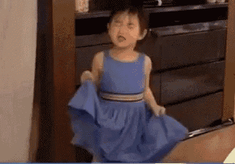 a little girl in a blue dress is standing in front of a dresser .