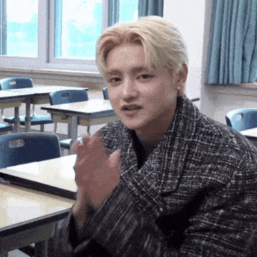 a young man in a plaid coat is clapping in a classroom