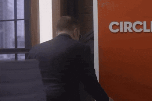 a man in a suit stands in front of a red sign that says circle