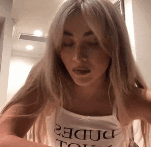 a woman with blonde hair is wearing a white tank top that says " rude " on it