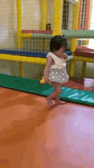 a little girl in a striped dress is walking on a trampoline .