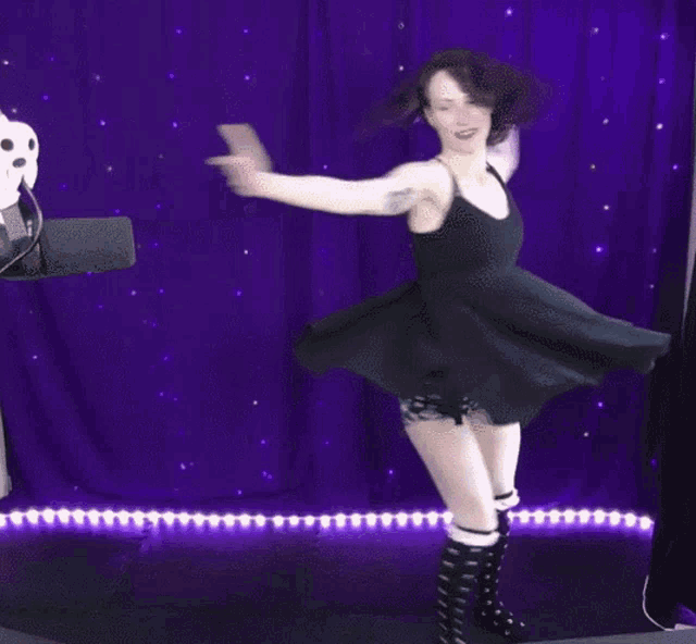 a woman in a black dress is dancing with her arms outstretched in front of a purple curtain .