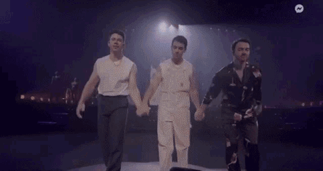three men are holding hands on a stage and dancing .