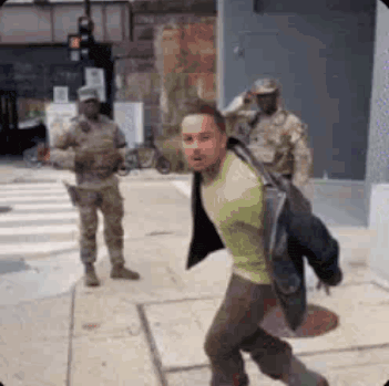 a man is being arrested by a group of soldiers on the street .