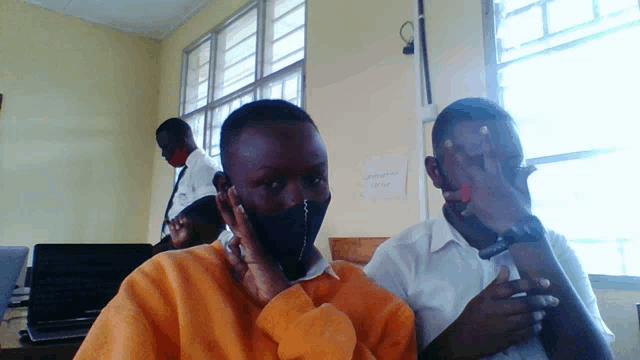 a man wearing a mask sits next to another man in front of a sign that says ' amanda ' on it