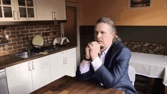 a man in a suit is sitting at a table in a kitchen