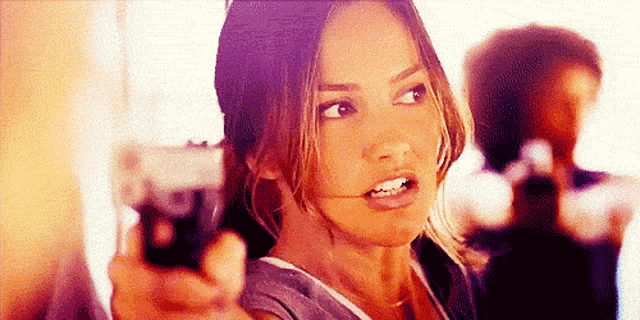 a woman is holding a gun in front of a man .