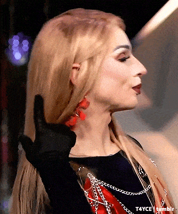 a woman with blonde hair and red earrings is wearing a black glove and giving a middle finger .