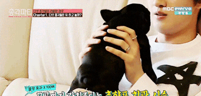 a man is holding a small black dog in his arms while watching mbc everyvo
