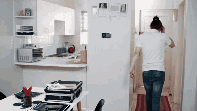 a woman in a white shirt walks through a kitchen with a clock on the wall that says ' i love you '