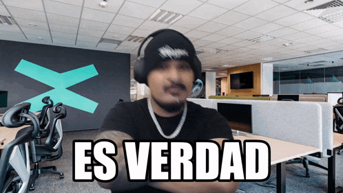 a man wearing headphones stands in an office with the words es verdad on the bottom