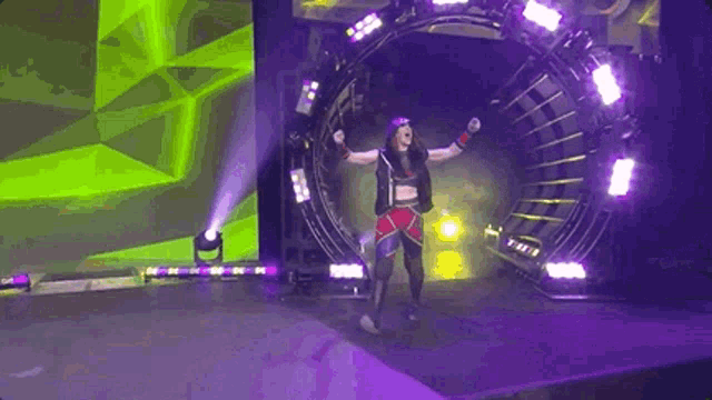 a female wrestler is walking through a tunnel on a stage with her arms in the air .