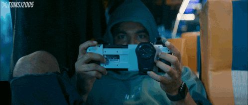 a man in a hoodie is taking a picture with a tomsj2005 watermark on the bottom right