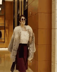 a woman wearing sunglasses and a fur coat is walking down a sidewalk .