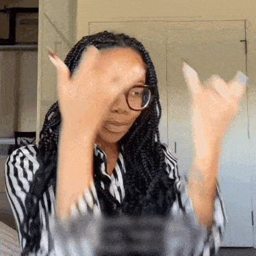 a woman wearing glasses and braids looks at herself in a mirror