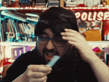 a man wearing a wig and glasses holds something in his hand in front of a shelf that says polis