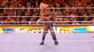 a woman is standing in a wrestling ring holding a pillow in front of a crowd .