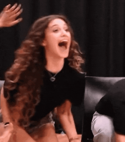 a woman with long curly hair is sitting on a chair with her mouth open .