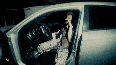 a man sitting in a car with a cup of coffee and a newspaper on his pants