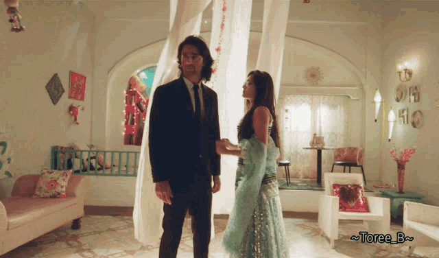 a man in a suit and tie stands next to a woman in a blue dress with the name toree b on the bottom right