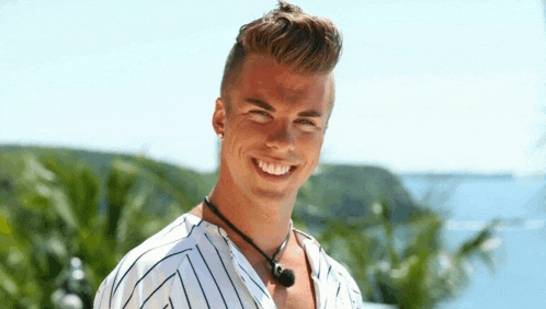a young man in a striped shirt is smiling in front of a body of water .