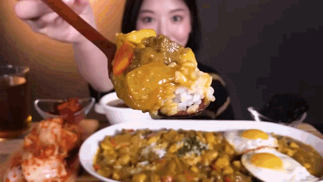 a woman is holding a spoon of curry over a plate of food .