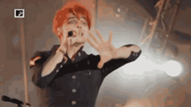 a man with red hair is singing into a microphone on stage .