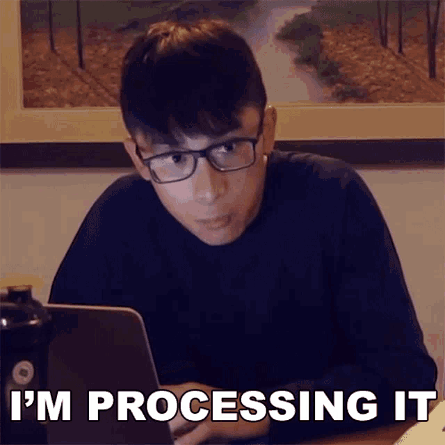 a man with glasses is sitting in front of a laptop with the words i 'm processing it on the screen