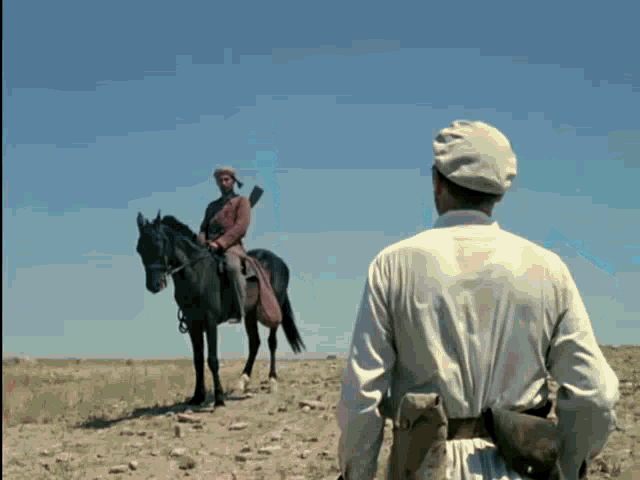 a man standing next to a man riding a horse in a field
