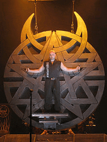 a man is standing in front of a huge symbol that says ' slayer ' on it