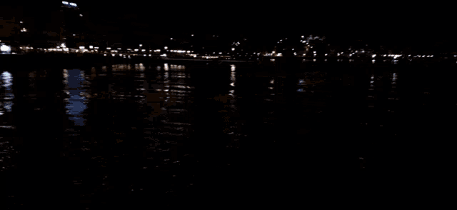 a blurry picture of a body of water at night with buildings in the background