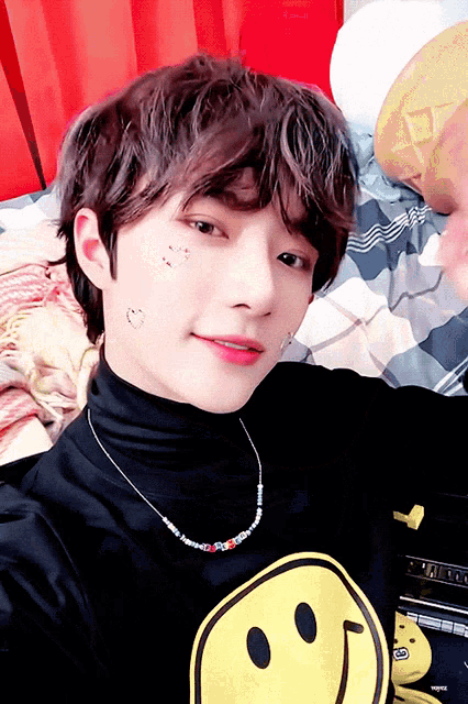 a young man wearing a black turtleneck and a necklace with a smiley face on it