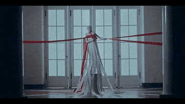 a woman in a long white dress with red ribbons around her