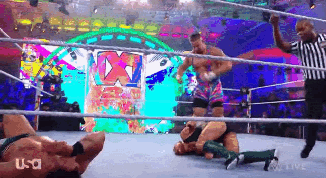 two men are wrestling in a wrestling ring with a referee in the background .