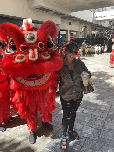 a woman stands next to a red lion mascot with the letter u on its head