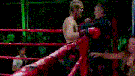 a woman is sitting in a boxing ring with a man in a boxing ring behind her .