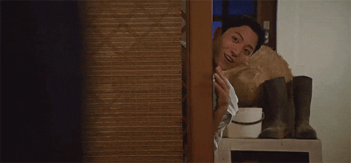 a man is peeking out from behind a door .