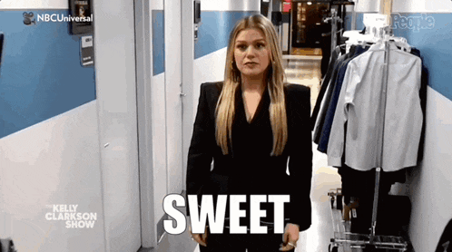 a woman in a black suit is standing in a hallway with the word sweet written on the floor .