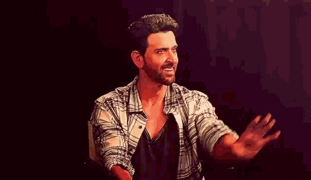 a man with a beard is sitting in a chair with his arms outstretched and smiling .