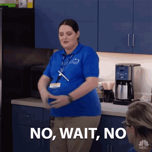 a pregnant woman in a blue shirt is standing in a kitchen and says no wait no