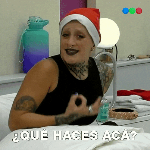 a woman wearing a santa hat is sitting on a bed and the words que haces aca are above her