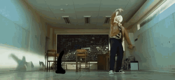a man in a tie is dancing in a classroom with a blackboard behind him