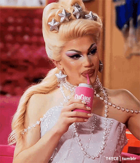 a woman in a white dress is drinking from a pink can that says rupaul on it