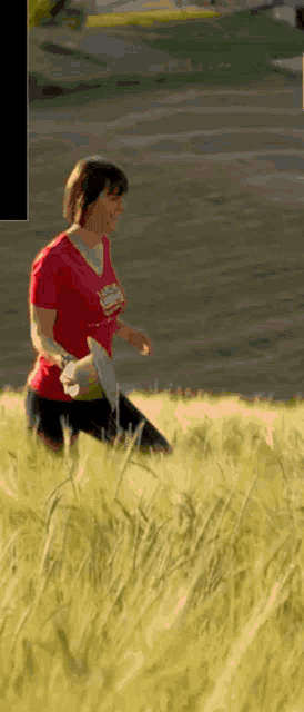 a woman in a red shirt is running through a field of tall grass